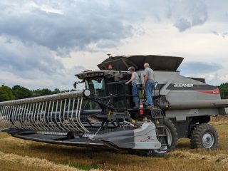 A wheat harvester and two farmers in their wheat field.